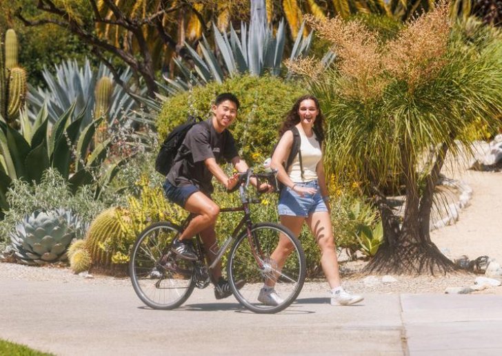 a student on a bike and a student walking smile while passing the grove house path