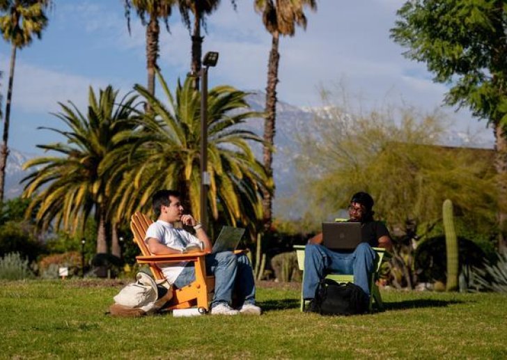 two students sit in chairs ont he mounds with the grove house behind them