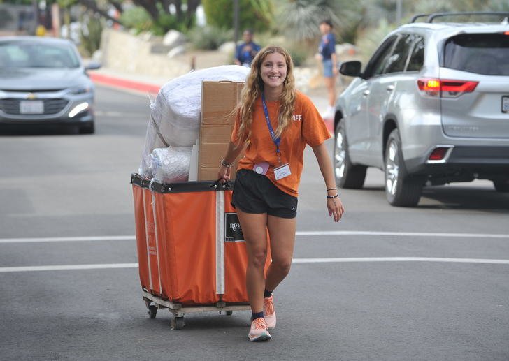 a student pulls an orange cart filled with items through a parking lot
