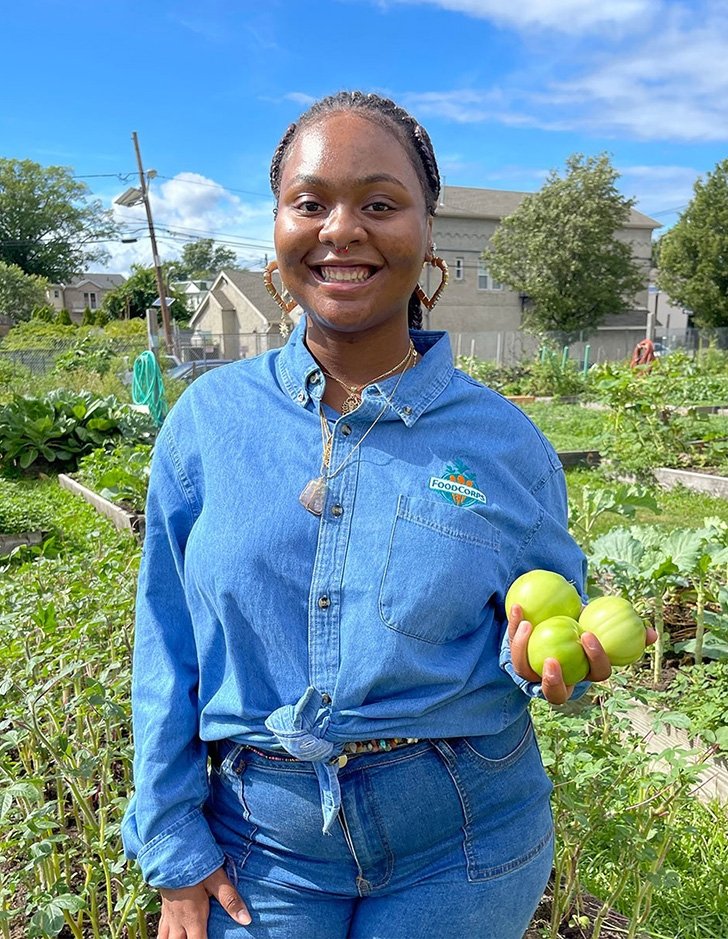 Yaquana Williams stands in a garden holding produce. 