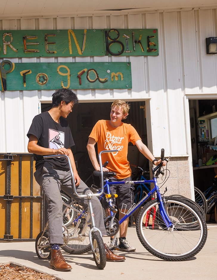 Students talk while sitting on bikes outside the Green Bike Program shed