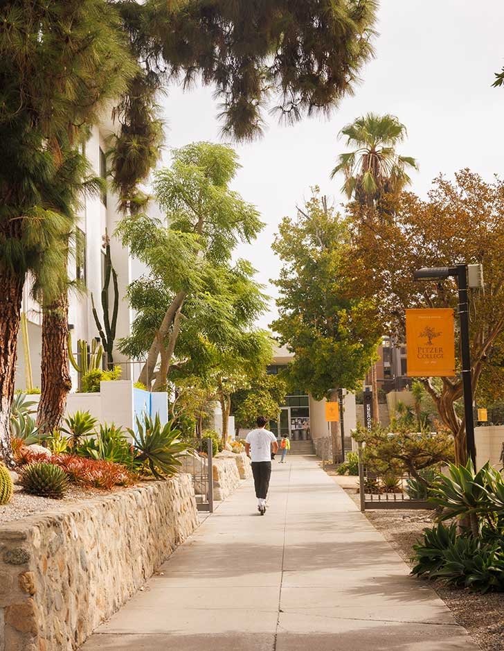 two students scooter towards gold student center on the pitzer walk