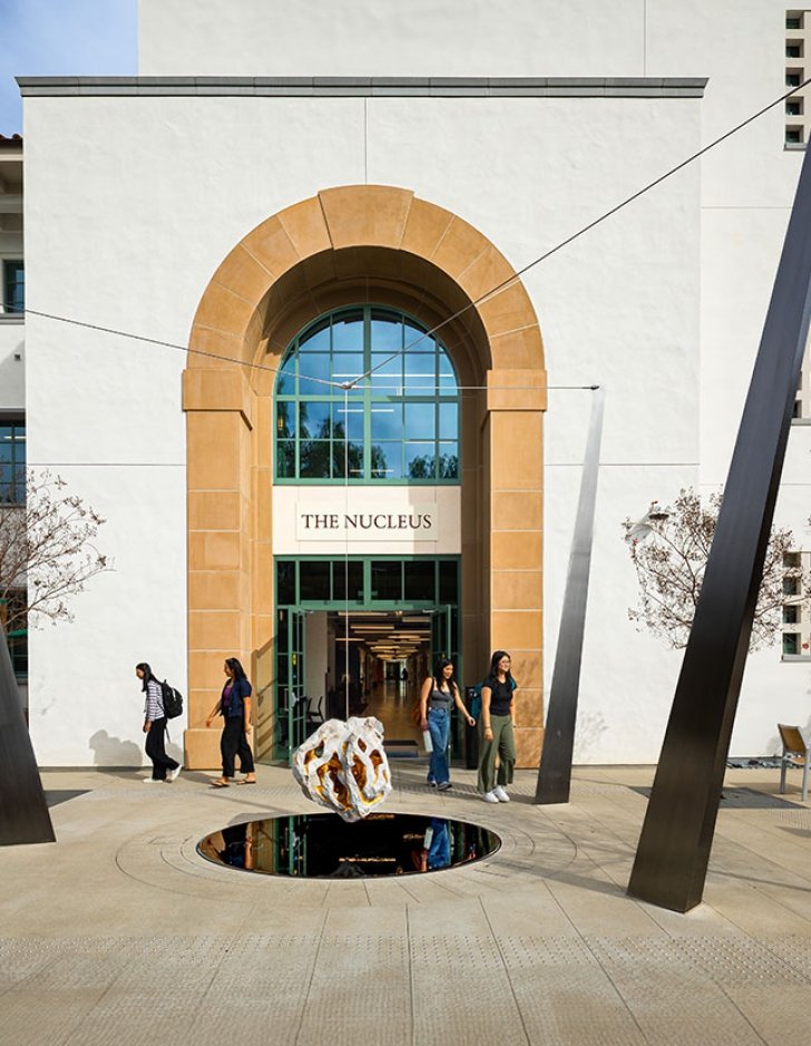 students walk past the arched entrance of the nucleus building on a bright day