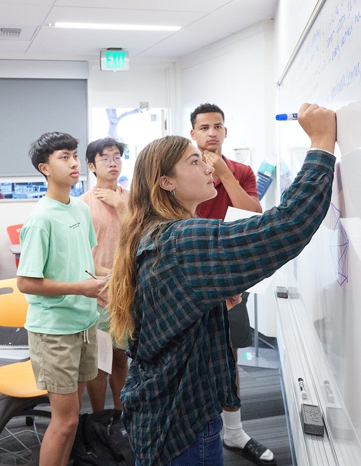 A Pitzer student completes a math problem as classmates look on