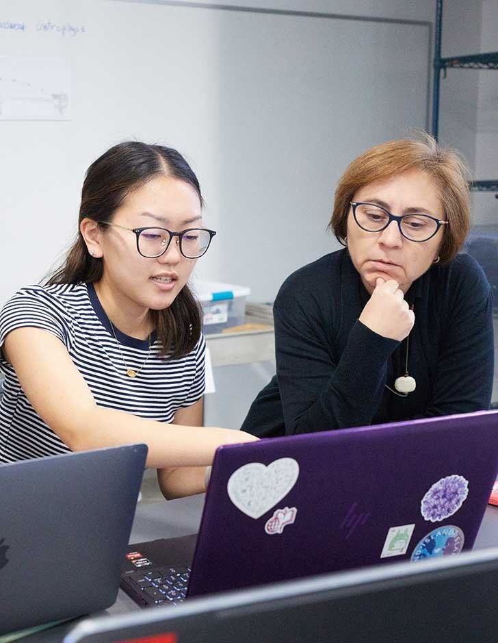 a student sits with a professor looking at a laptop