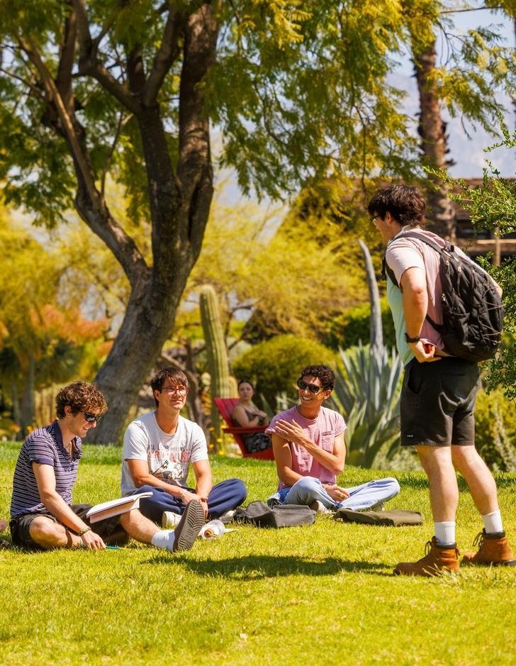 four students socialize on the grass of the mounds