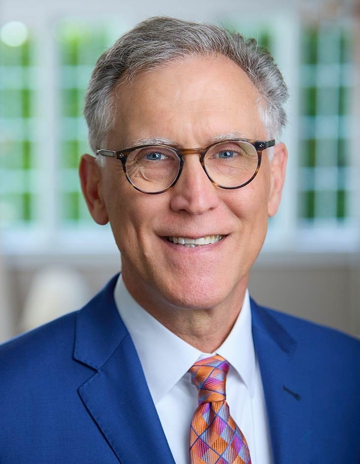 headshot of pitzer president strom Thacker wearing a blue suite, glasses, and colorful tie