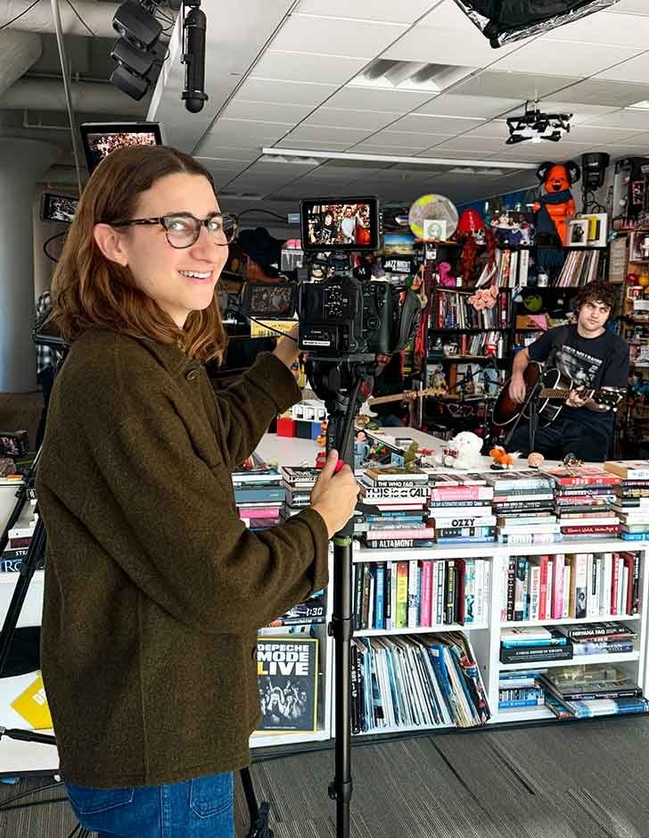 Maia Stern stands at a camera focused on a band at NPR's Tiny Desk Concert set