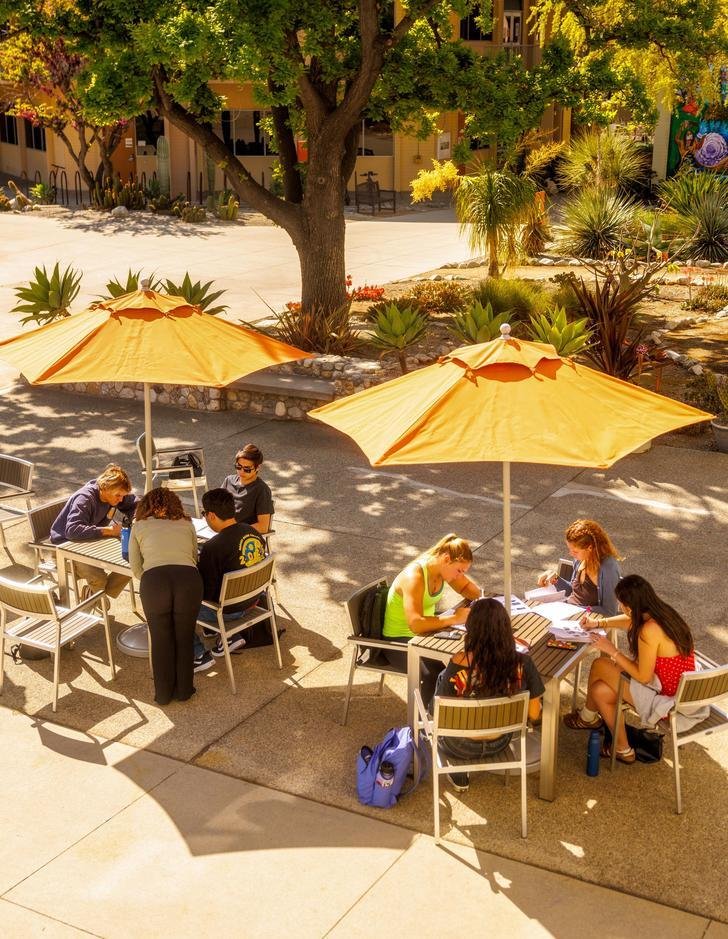 several students sit at two umbrella tables on scott courtyard
