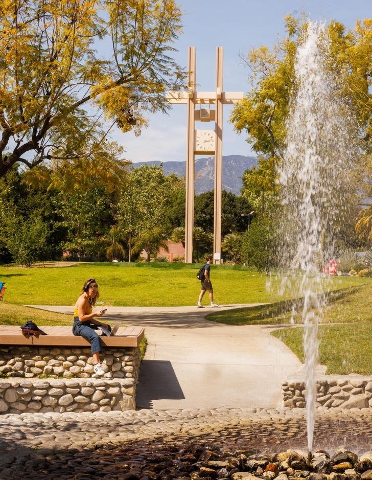 a student sits on the dock of the pitzer fountain with the clock tower in the distance