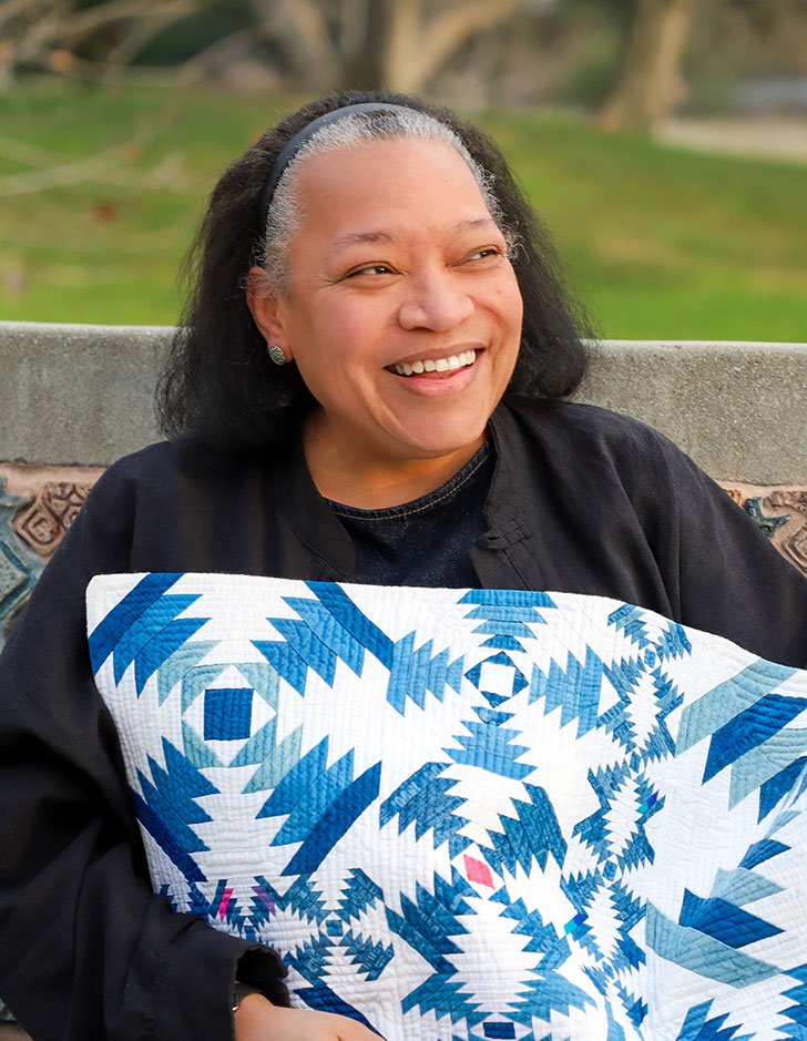 Chawne Kimber sits on a bench while holding one of her quilts