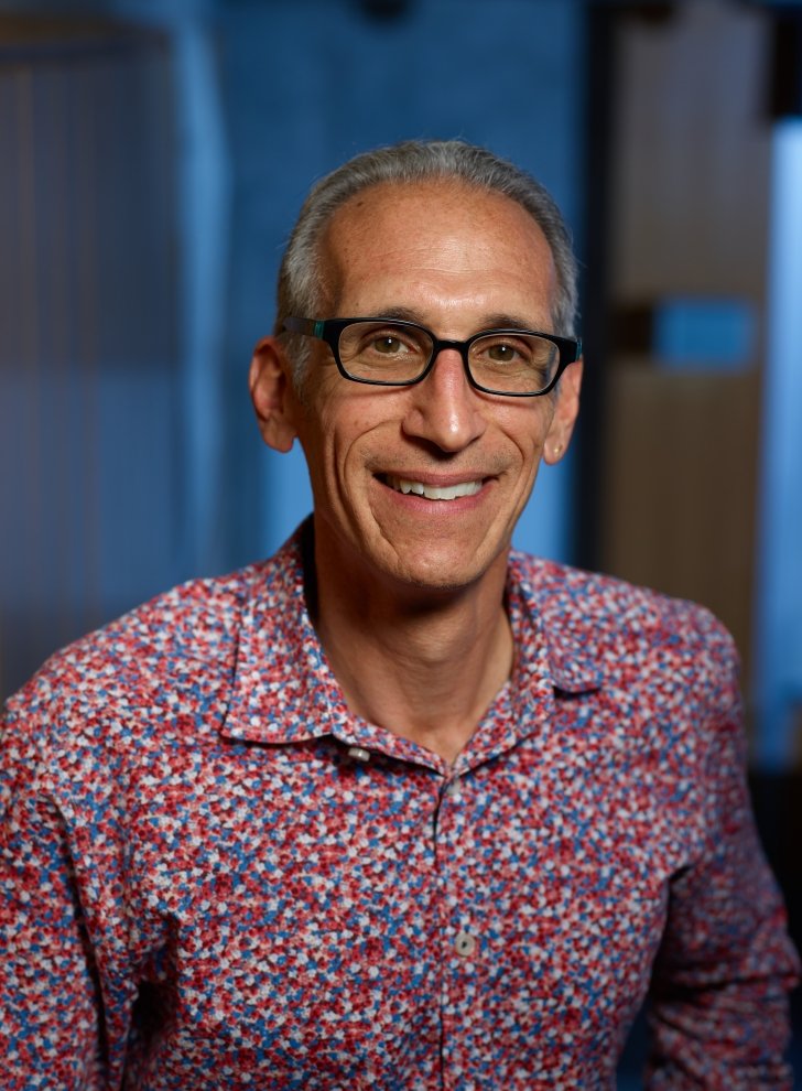 Man, smiling, with gray hair, wearing glasses, and patterned collared shirt.
