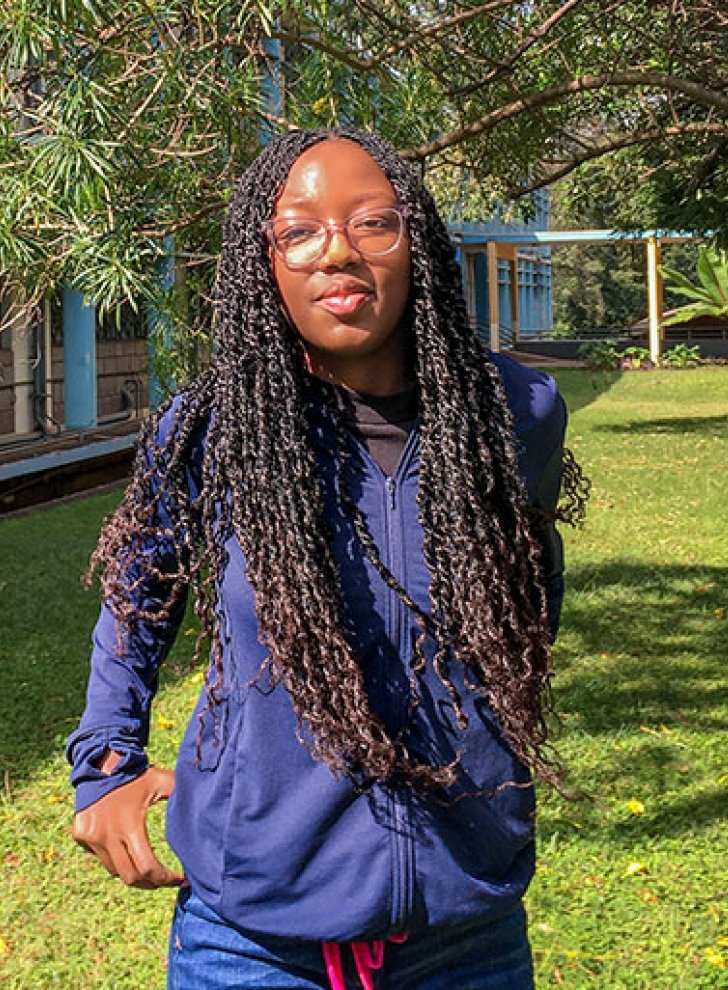 Sia Were wears a navy blue jacket and glasses and has long black hair in braids.