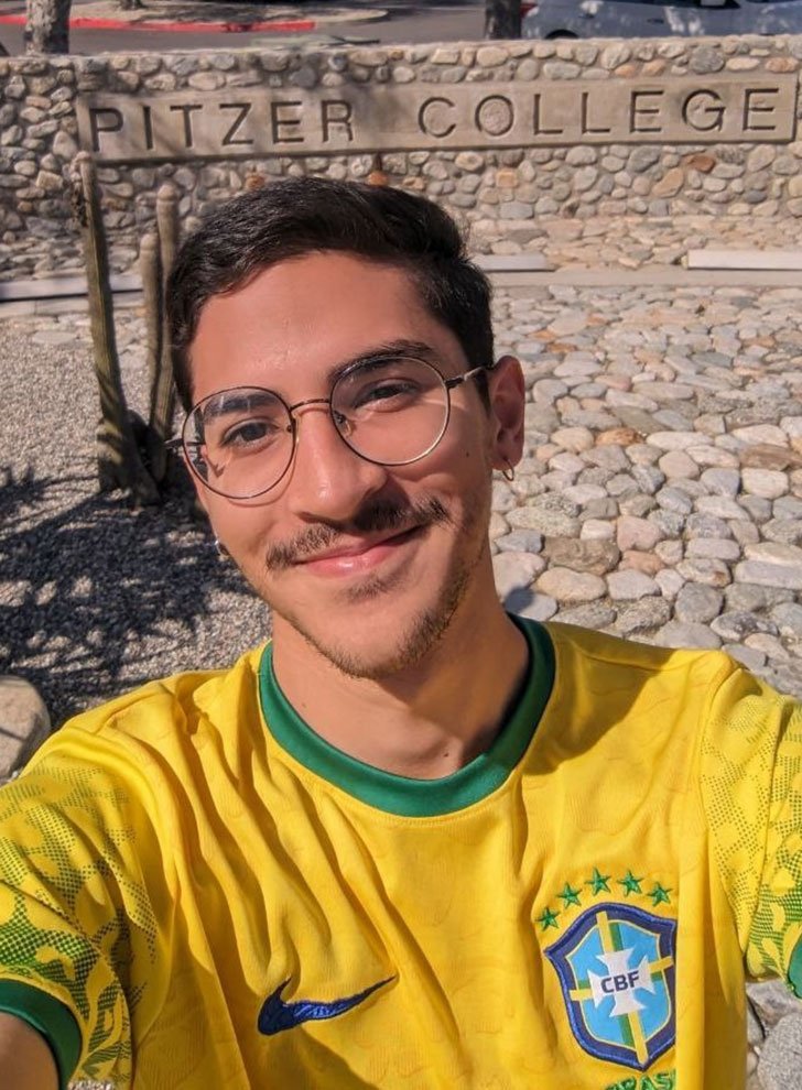 portrait of Joao Vitor de Lima wearing a Brazilian football jersey posed in front of the Pitzer College stone sign