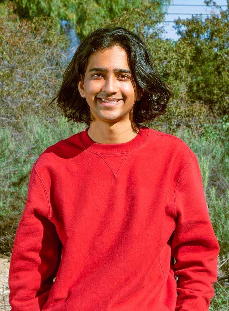 tommy shenoi wears a bright red sweater while posing in Pitzer outback