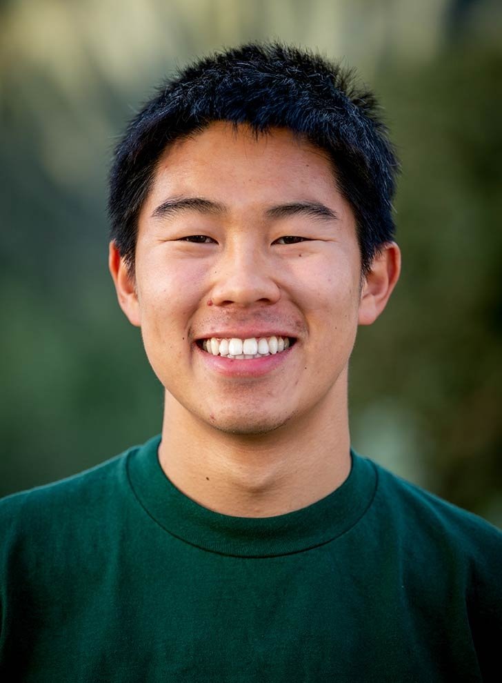 headshot of carter soe, posing in front of a green background, wearing a green tshirt