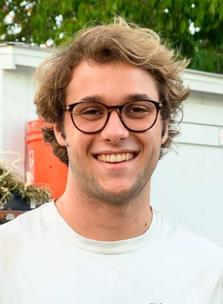 a student wearing glasses and a white tshirt smiles at the camera