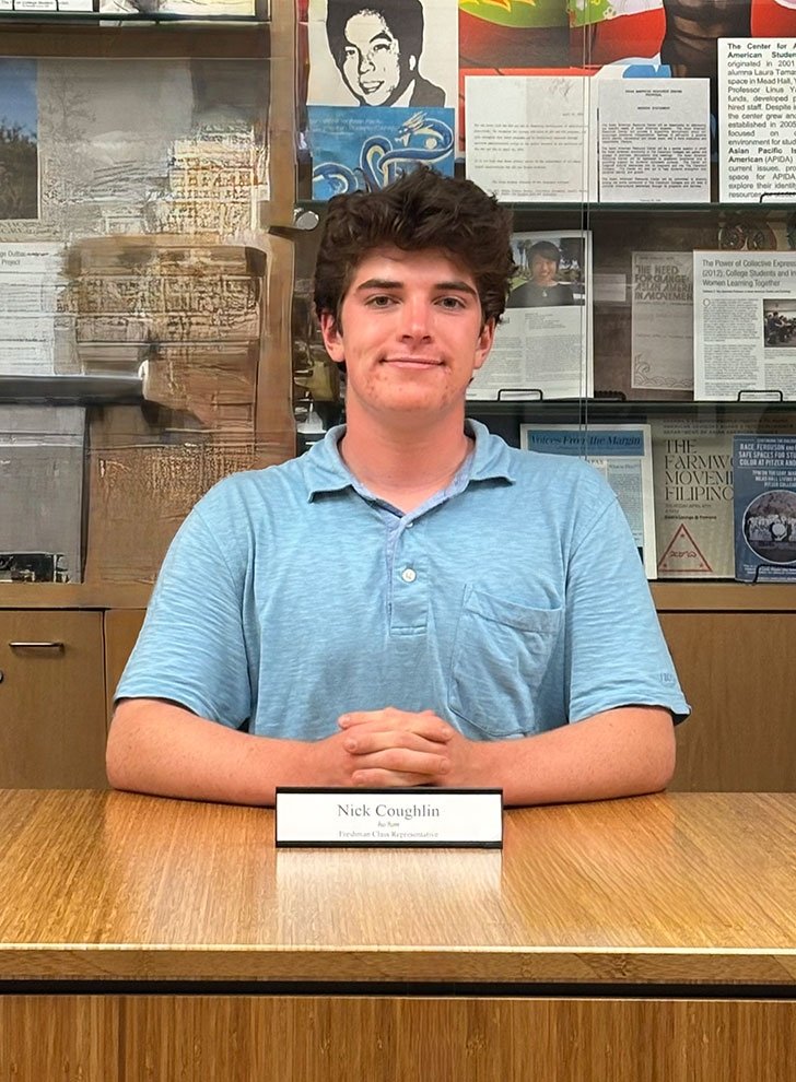 nick coughlin sits at a conference table with his name plate in front of him