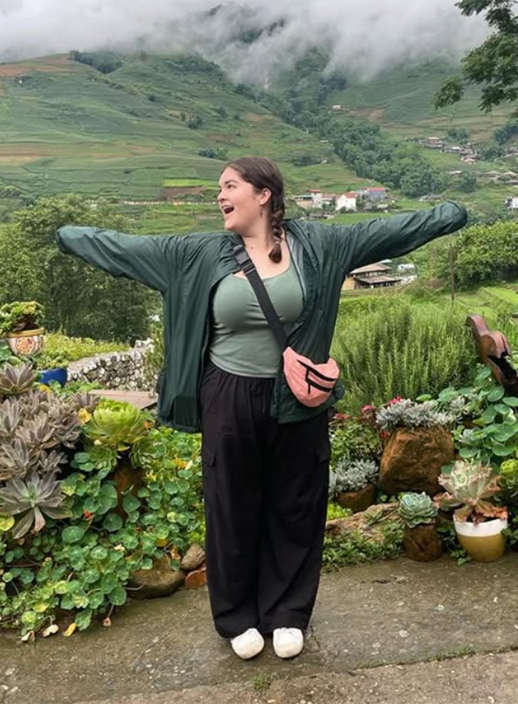 brynn anderson stands on a path with a lush landscape behind her