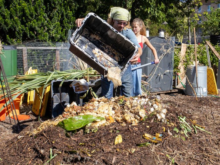 a student dumps food waste into the student garden compost heap