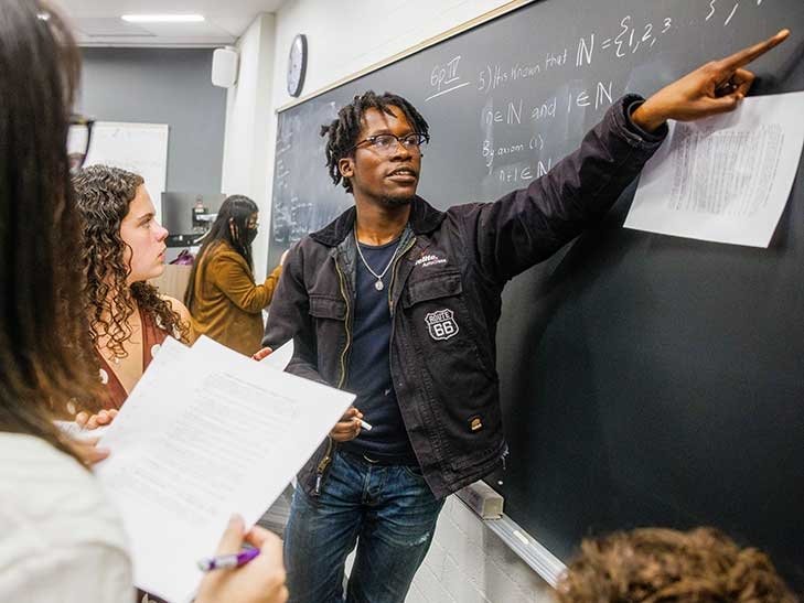 a student points to writing on a blackboard in a classroom during group work