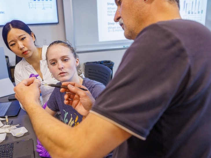 A biology professor performs a demonstration for two students