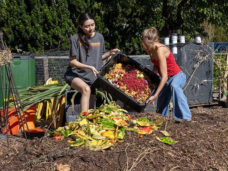 two students dump food scraps onto a compost pile in the pitzer student garden