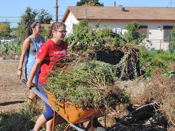 student moves a large wheelbarrow filled with weeds at Huerta del Valle