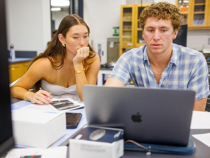 two students work together at a laptop station in a science lab