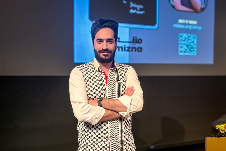 Yahya Ashour stands on the Benson Auditorium stage while wearing a shirt with a black and white keffiyeh pattern.