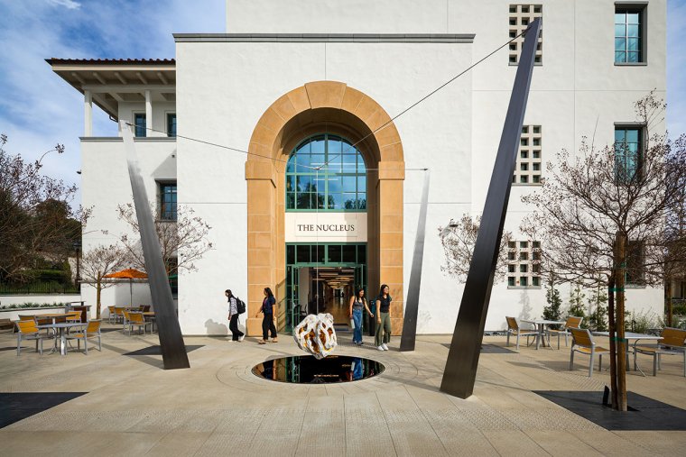 students walk past the arched entrance of the nucleus building on a bright day