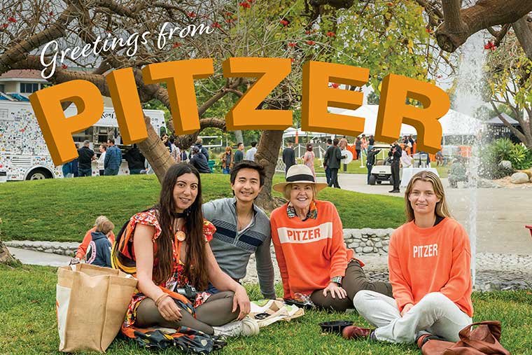 four alumni sit on the mounds with the fountain behind them with the words "Greetings form Pitzer" above them in orange