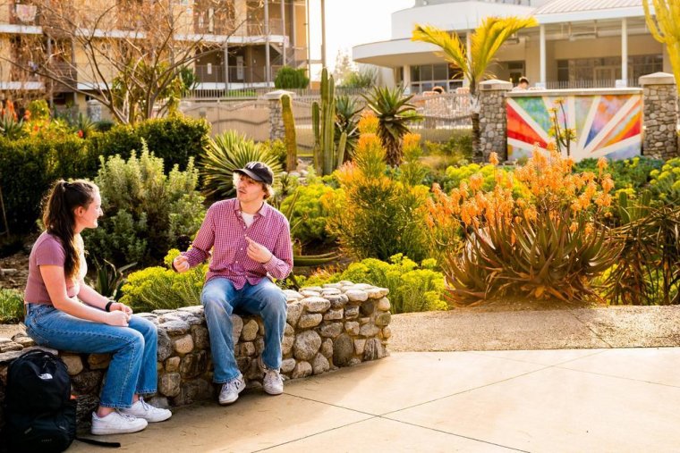 two students sit on a wall conversing near the Pitzer dorms
