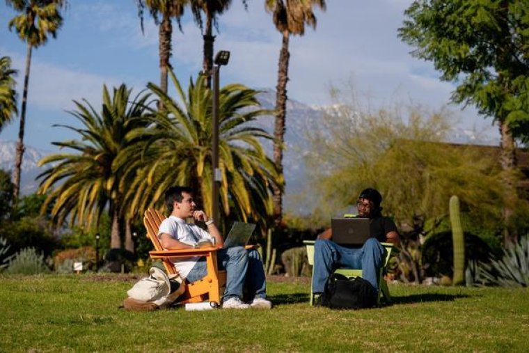 two students sit in chairs ont he mounds with the grove house behind them