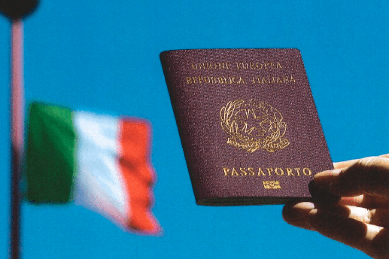 a hand holds an Italian passport with the Italian flag flying in the background