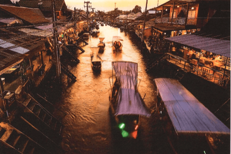 Boats float on a canal in Thailand at sunset