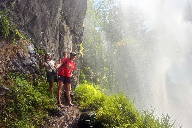 three students hike under a waterfall