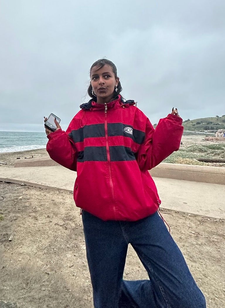 feven aklilu wearing a red and blue parka poses on the beach