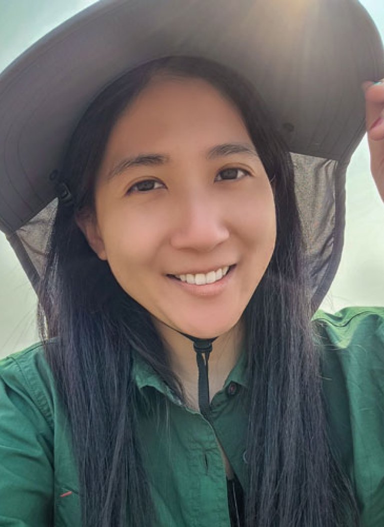 Closeup of Jo Ann Wang, who has long straight black hair and weras a green collared shirt and a wide-brimmed white hat.
