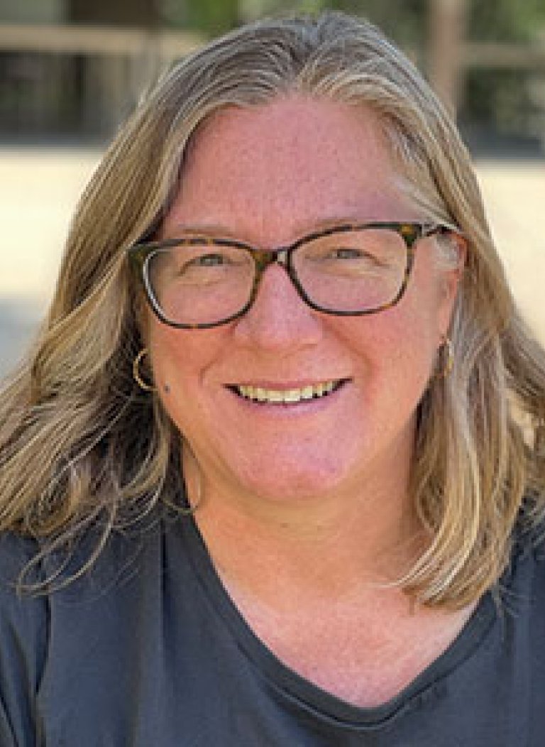 a woman with shoulder-legnth blond hair wears black glasses ad a blue tshirt