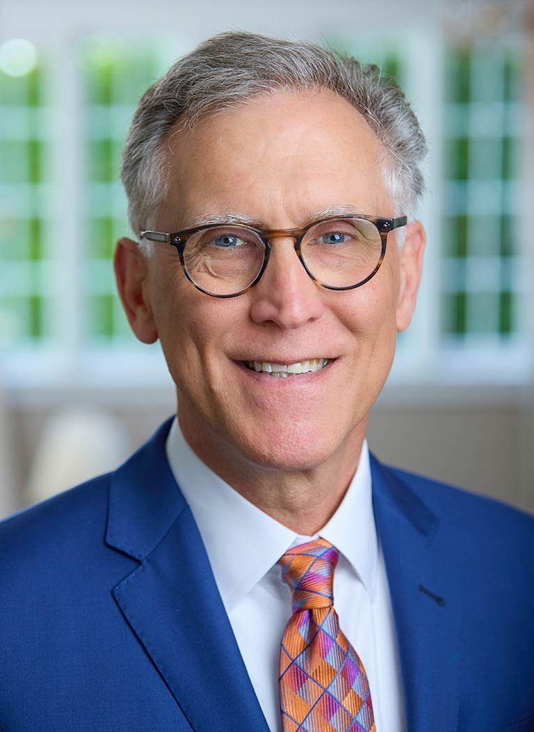 portrait of strom thacker wearing a blue suit, glasses and a colorful tie