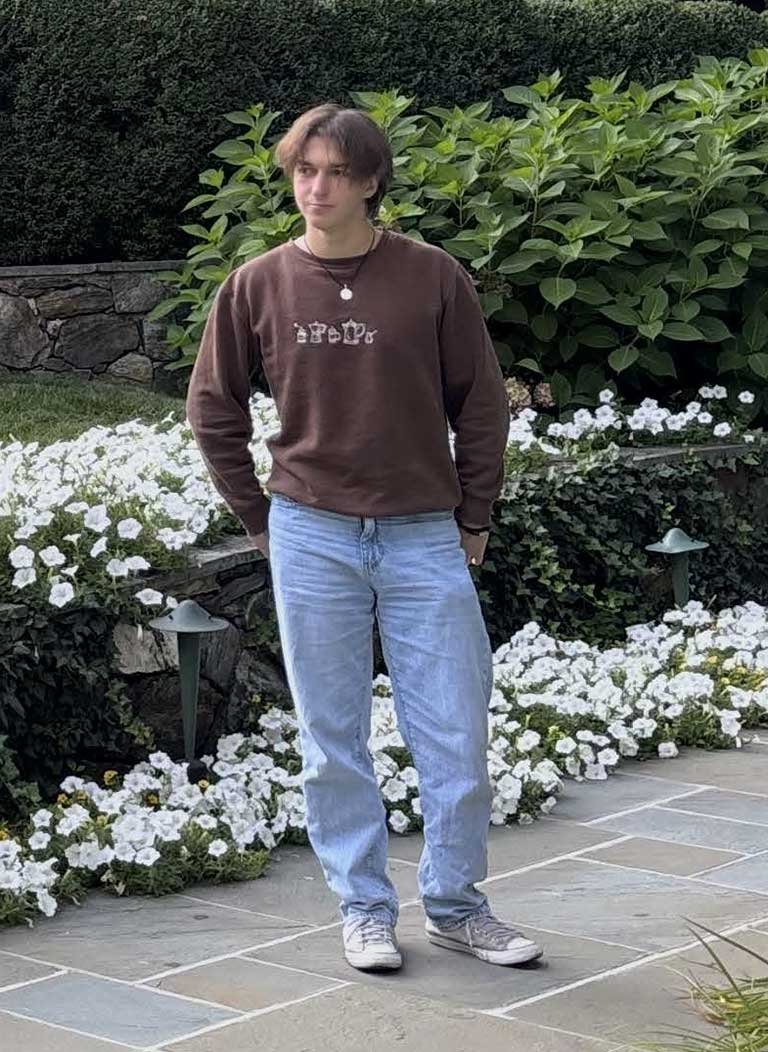 Man standing wearing brown sweater and blue jeans.