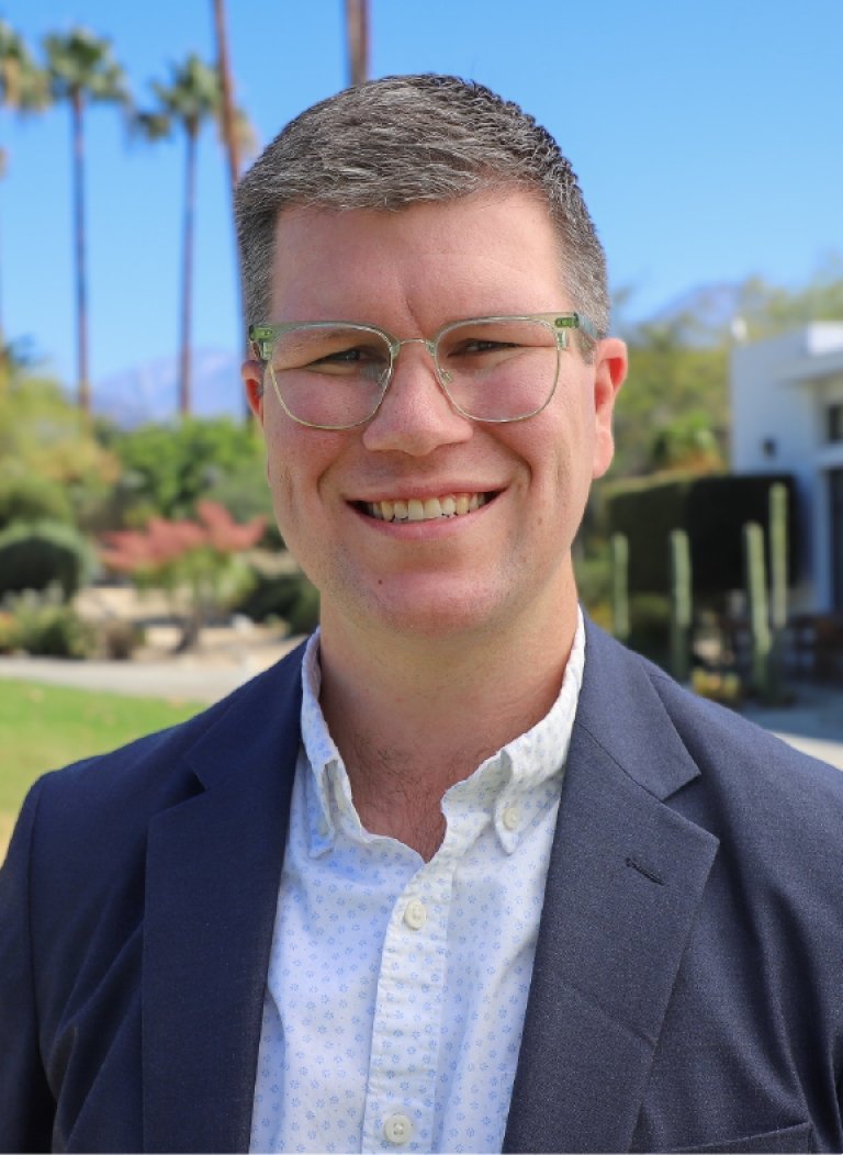 Man wearing navy colored suit with glasses and short brown hair.
