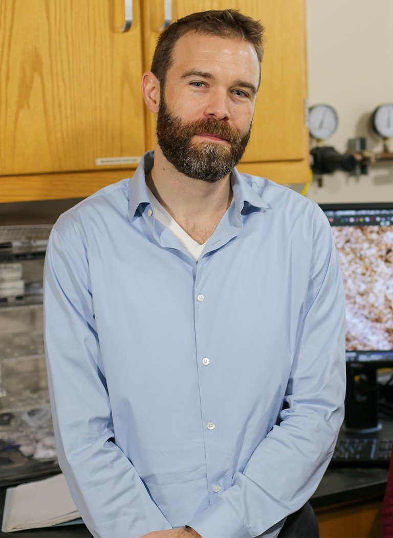 Man in blue button up with short brown hair and beard.