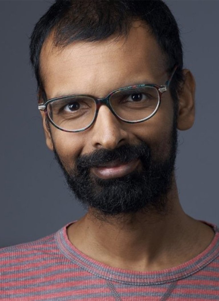 Man with short black hair wearing black glasses and red t-shirt.