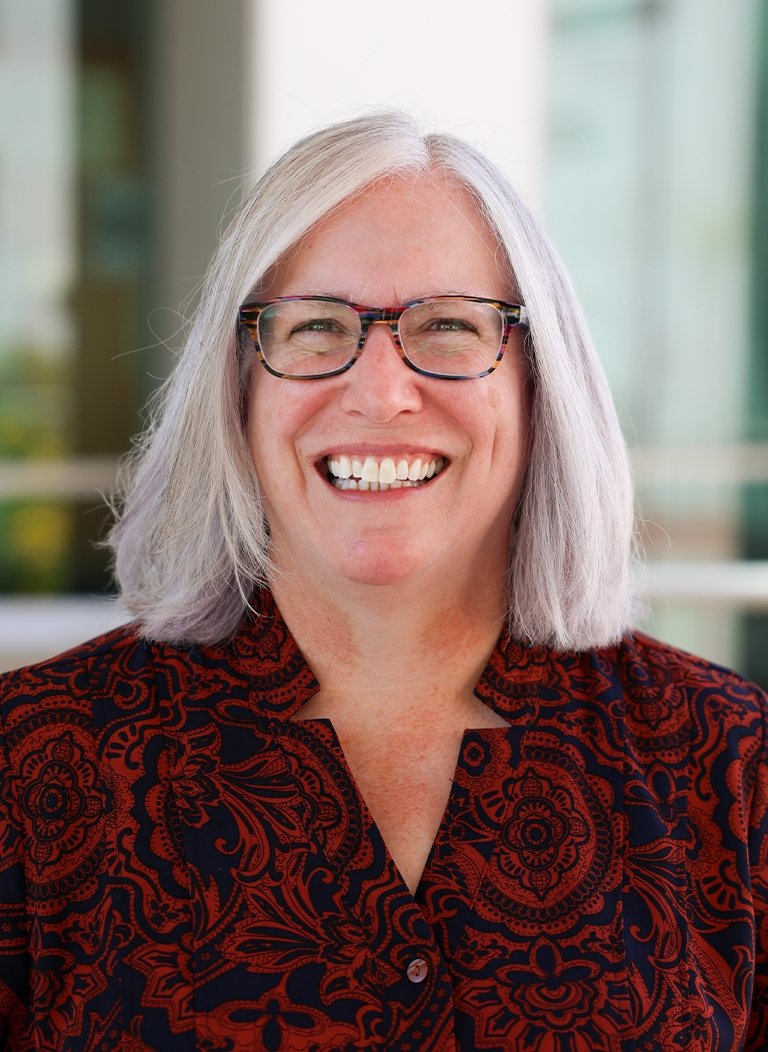 Woman wearing red blouse and glasses with short white hair.