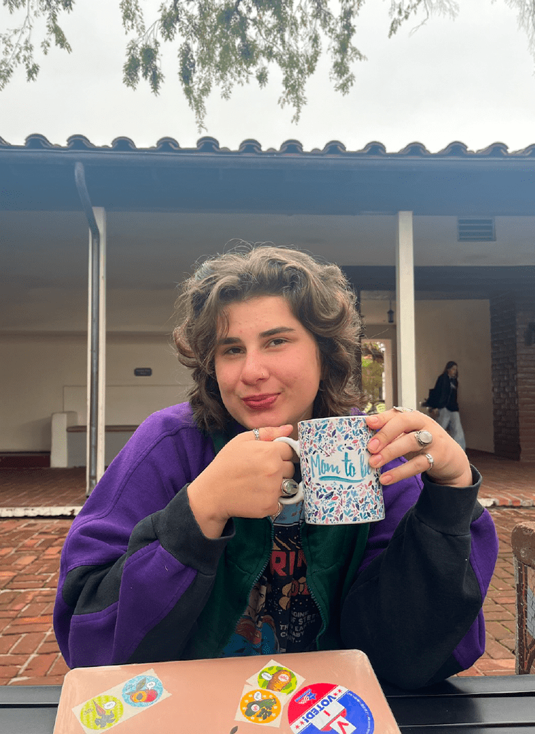 Woman with short brown hair wearing purple jacket and holding mug.