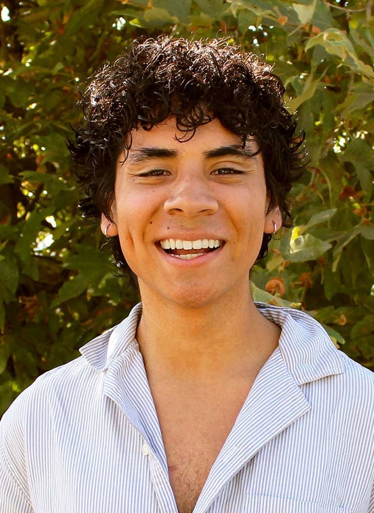 head shot of Nick Hernandez standing in front of outdoor greenery