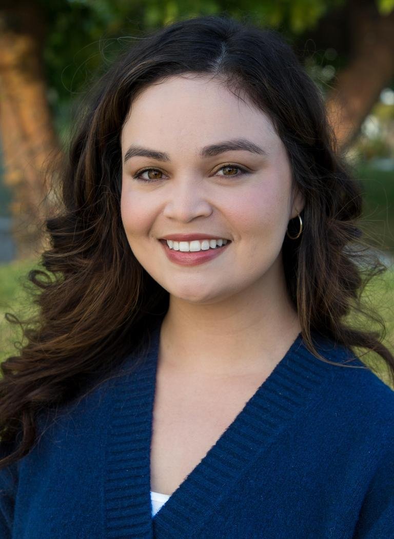 Woman in blue sweater with long curly dark brown hair.