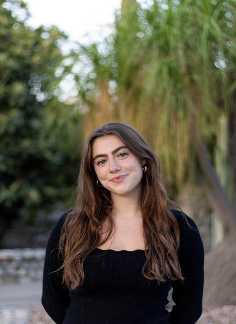 a girl with long brown hair in a black top with trees in the background